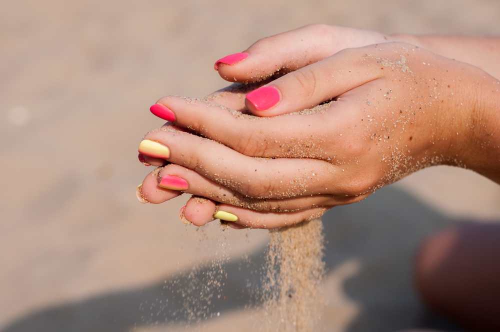 момиче държащо пясък в ръце с красив розов маникюр